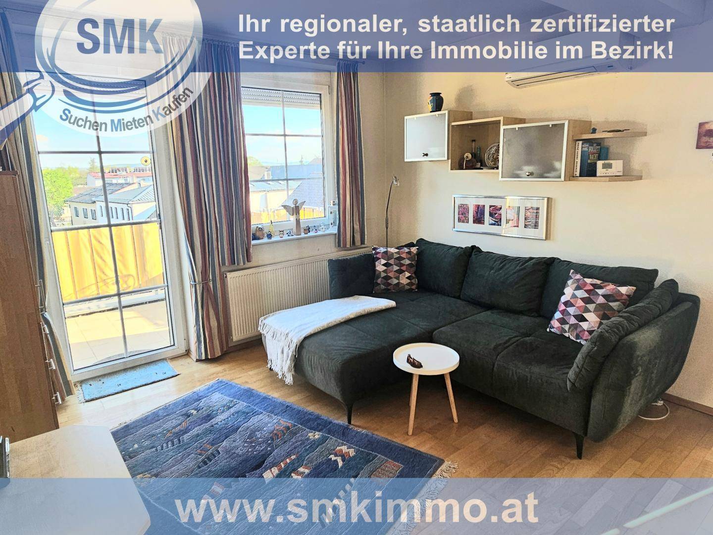 Gemütliches Wohnzimmer mit dunklem Ecksofa, Teppich und Zugang zu einem Balkon.