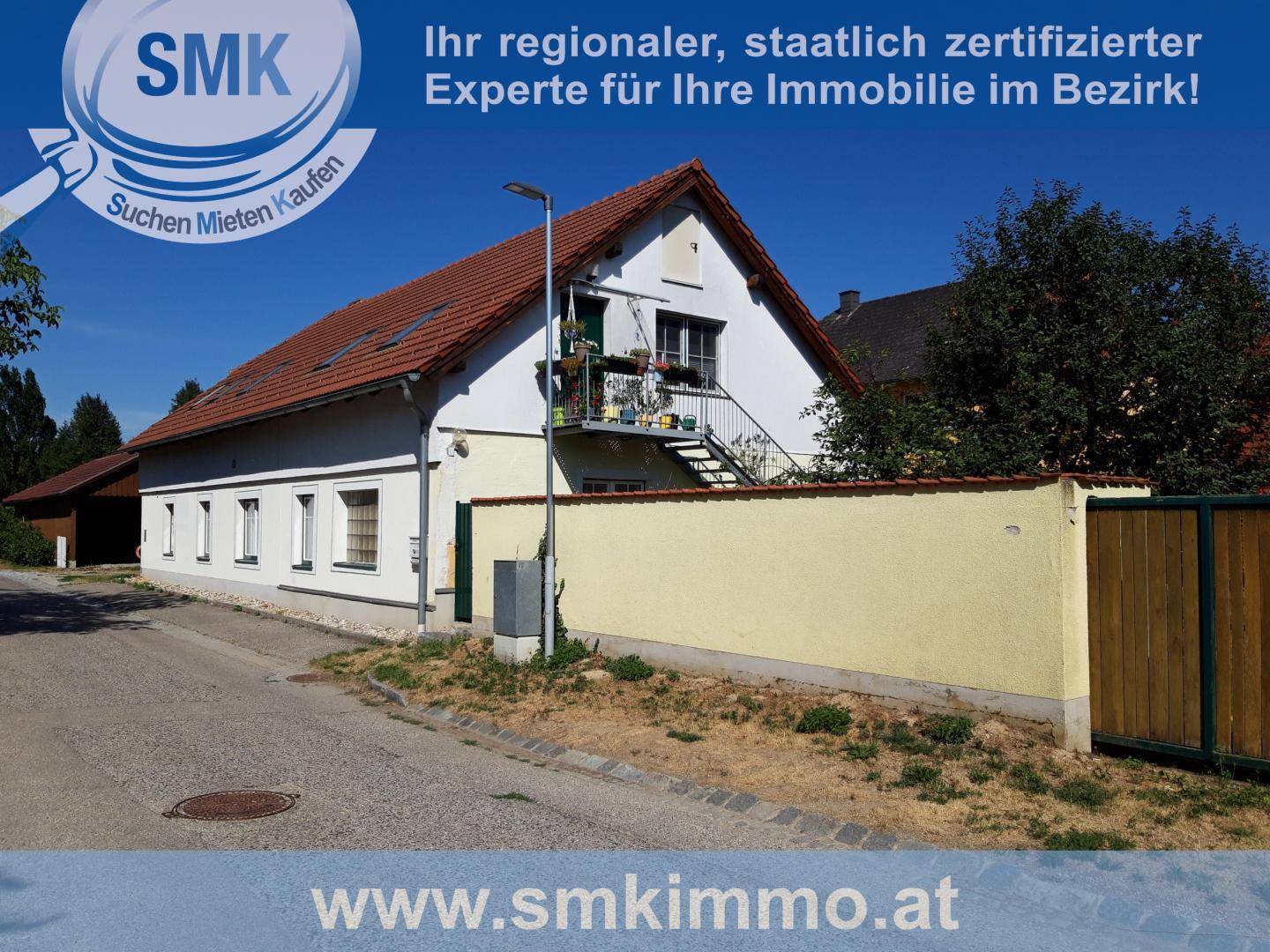 Ansicht des Gebäudes von der Straße aus mit einer niedrigen Mauer und einer Außentreppe.