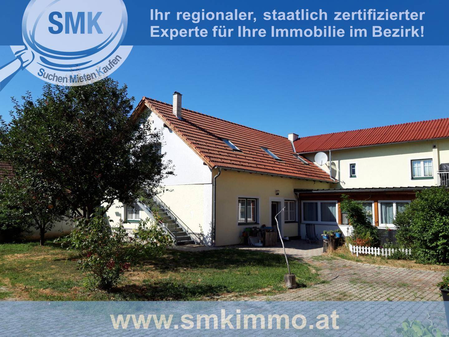 Seitenansicht des Gebäudes mit rotem Ziegeldach, Außentreppe und einem gepflegten Gartenbereich.