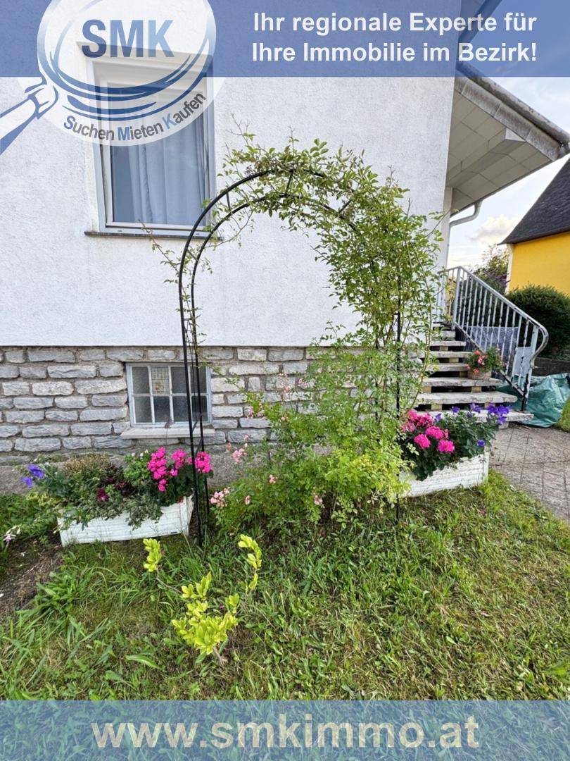 Seitlicher Gartenbereich des Hauses mit Blumenbeeten, einer Rankhilfe und Außentreppe.