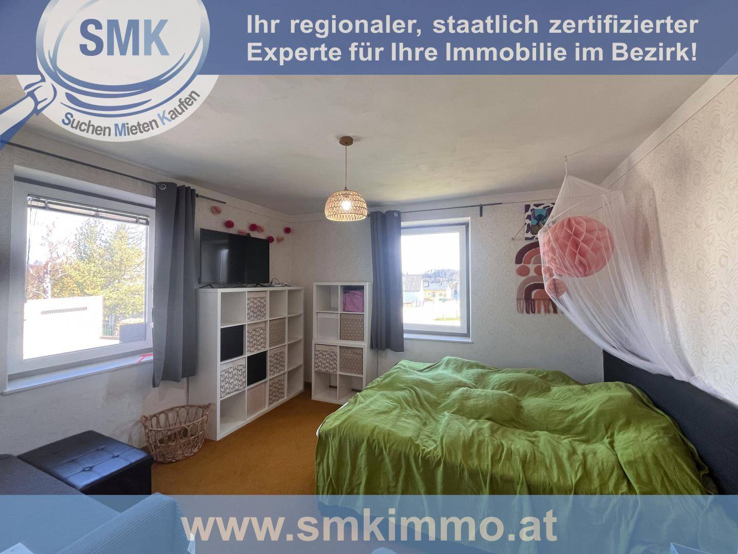 Gemütliches Schlafzimmer mit einem großen Bett, Regalen und zwei Fenstern für natürliches Licht.