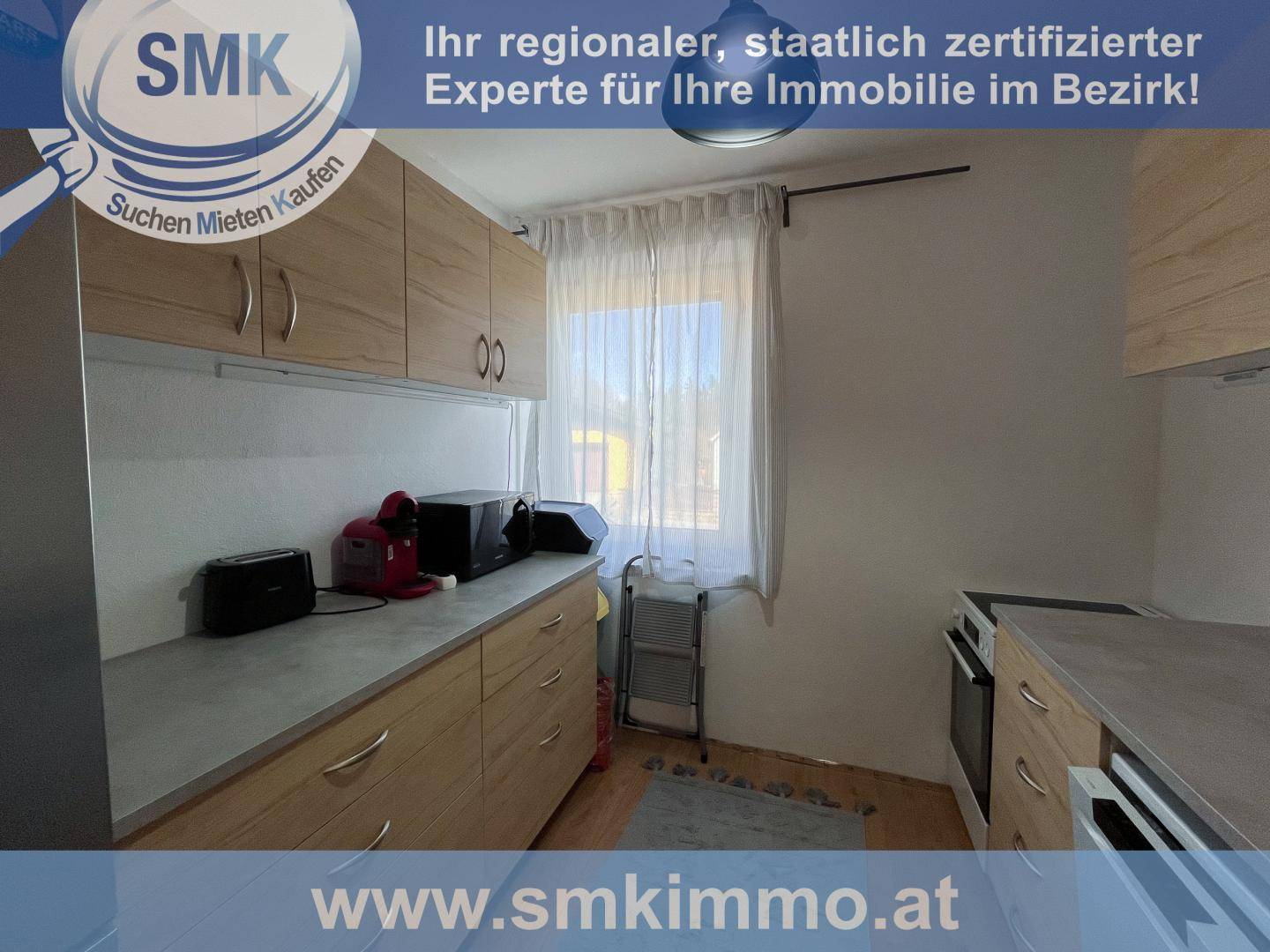 Funktionale Küche mit hellen Holzschränken, Arbeitsplatte und einem Fenster mit Vorhängen.