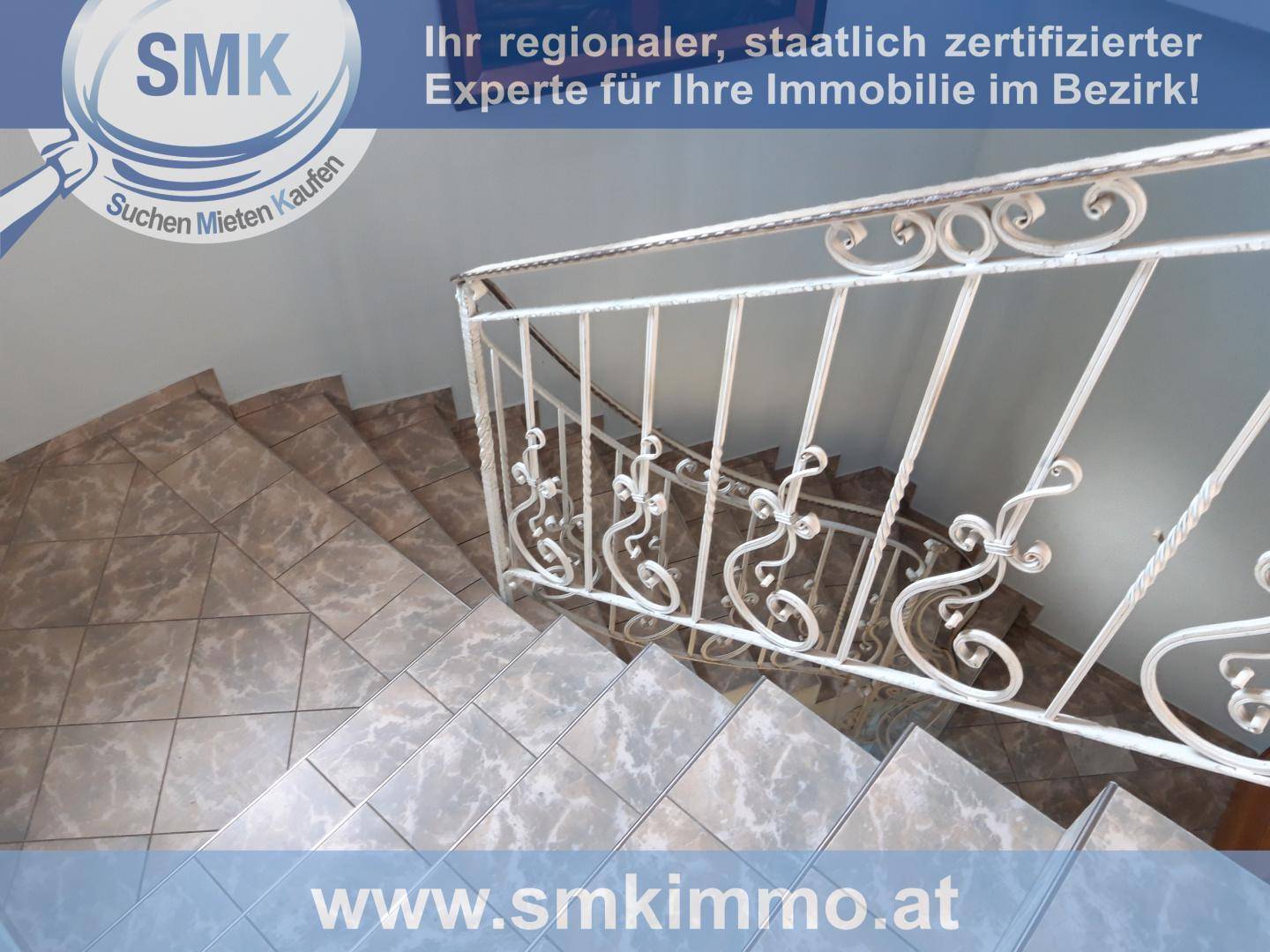 Blick von oben auf eine geflieste Treppe mit kunstvollem weißen Metallgeländer.