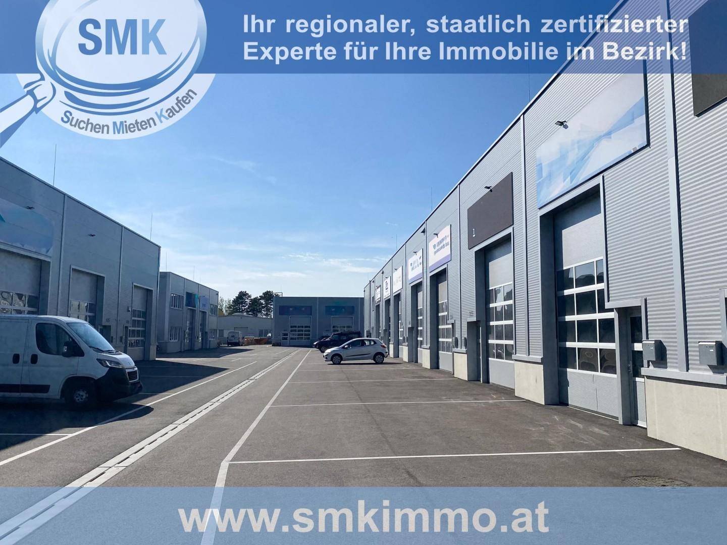 Reihe moderner Gewerbegebäude mit zahlreichen Parkplätzen und breiter Zufahrtsstraße unter blauem Himmel.