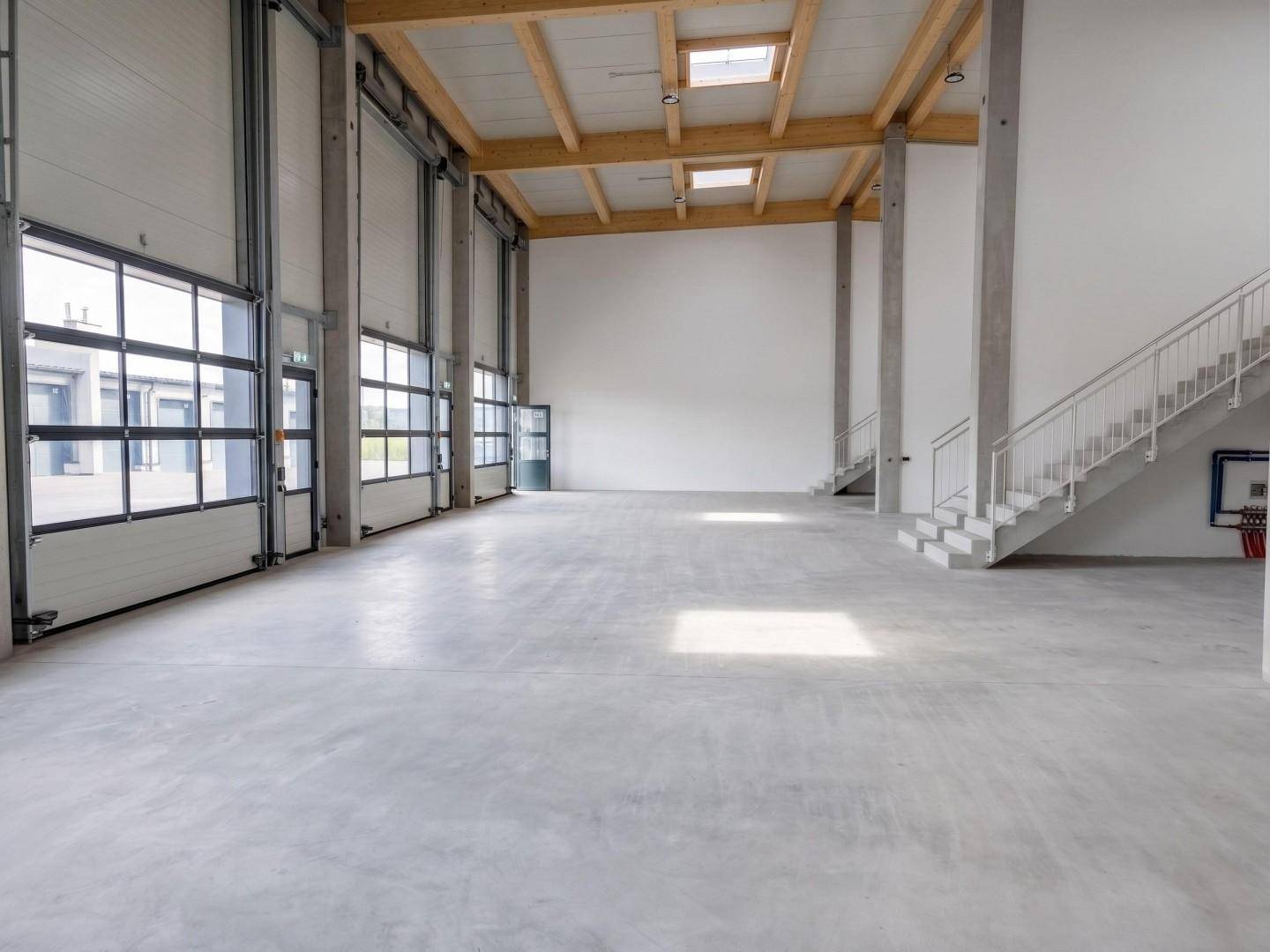 Helle Gewerbehalle mit mehreren großen Rolltoren, hohen Decken und Betonboden.