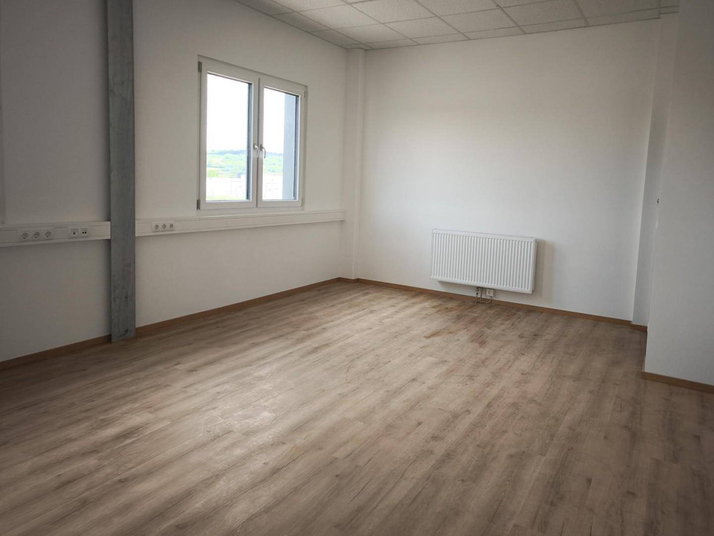 Leeres Büro mit Laminatboden, weiß gestrichenen Wänden und einem großen Fenster.