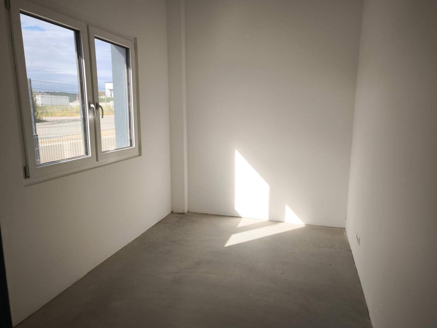 Leerer Raum mit weiß gestrichenen Wänden, Betonboden und einem Fenster.