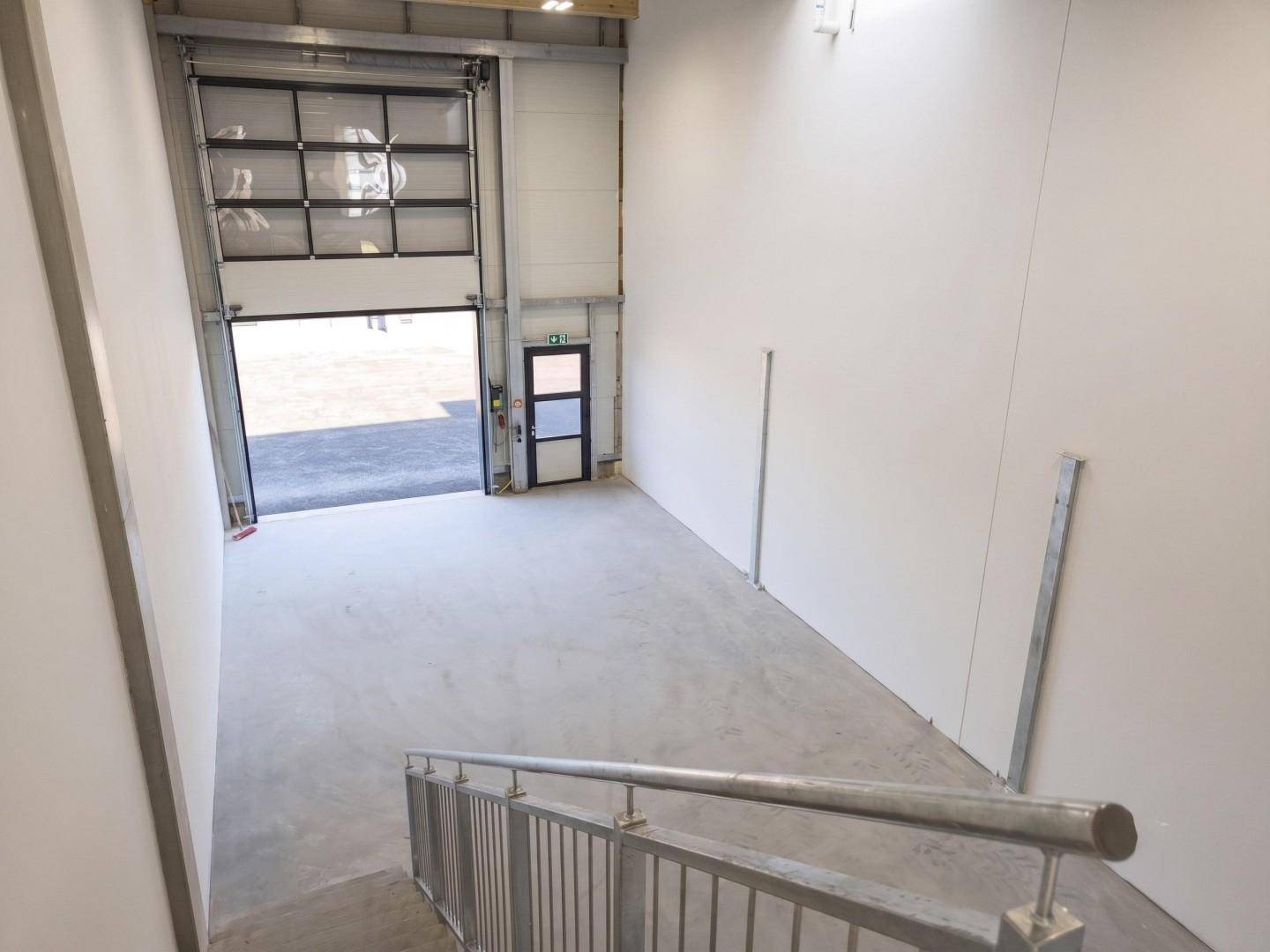Blick von der Treppe in eine Gewerbehalle mit großem Rolltor und Zugang zum Außenbereich.
