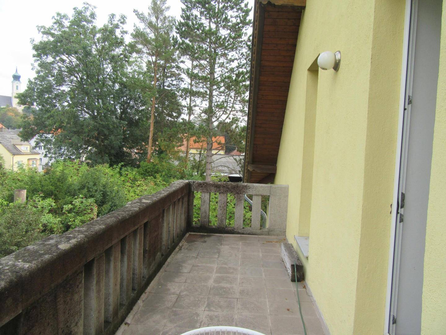 Geräumiger Balkon mit Steinbrüstung und Blick auf die Umgebung und einen Kirchturm.