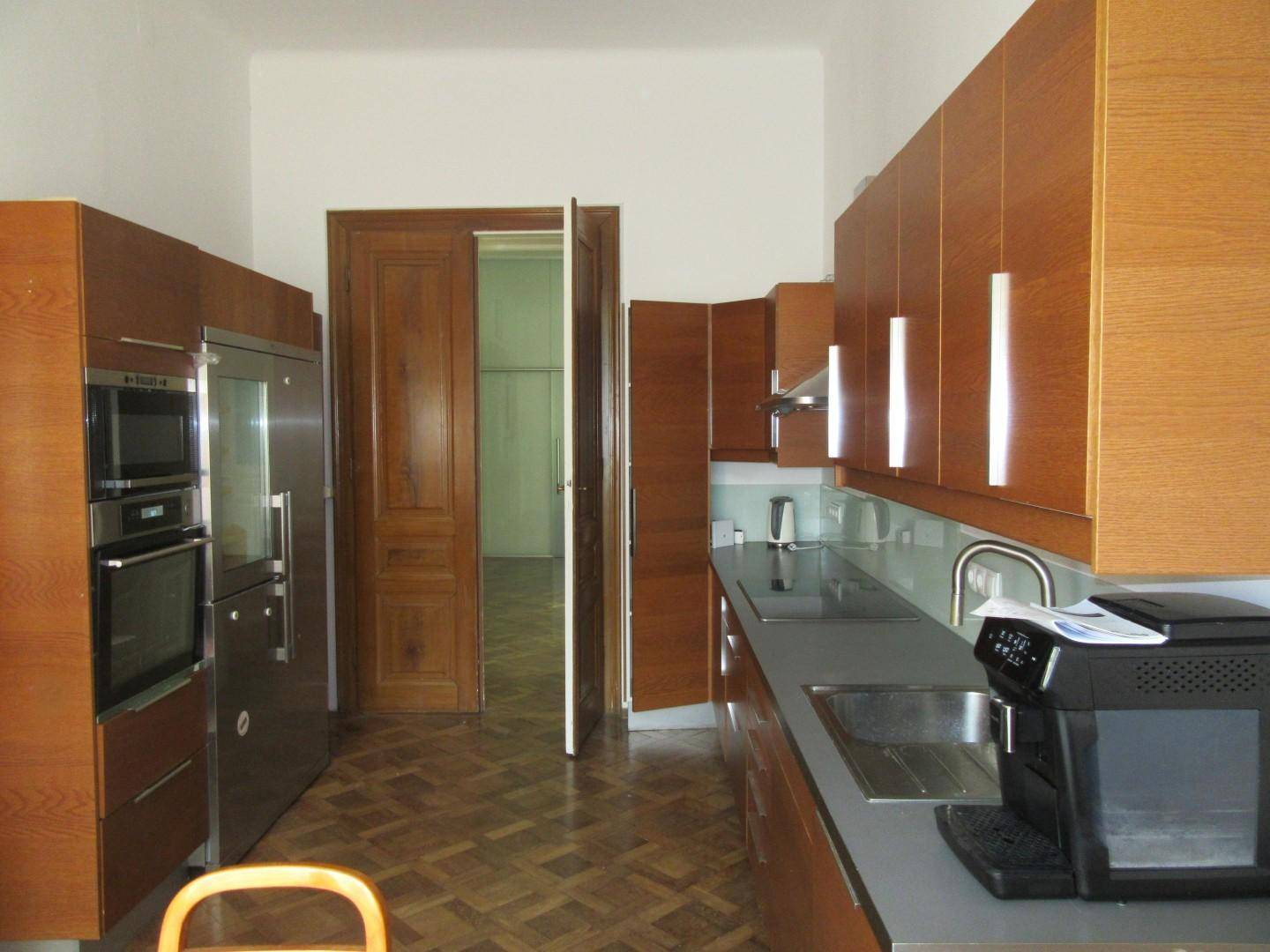 Funktionale Küche mit Holzschränken, modernen Geräten und Parkettboden, gut beleuchtet.