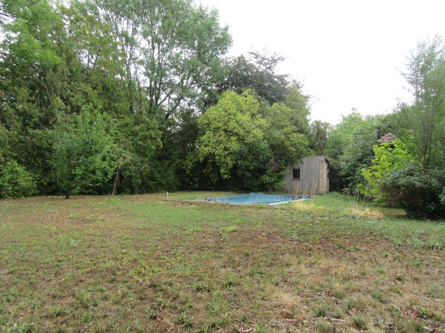 Garten mit Rasenfläche, einem kleinen Pool und einem Gartenschuppen, umgeben von Bäumen.