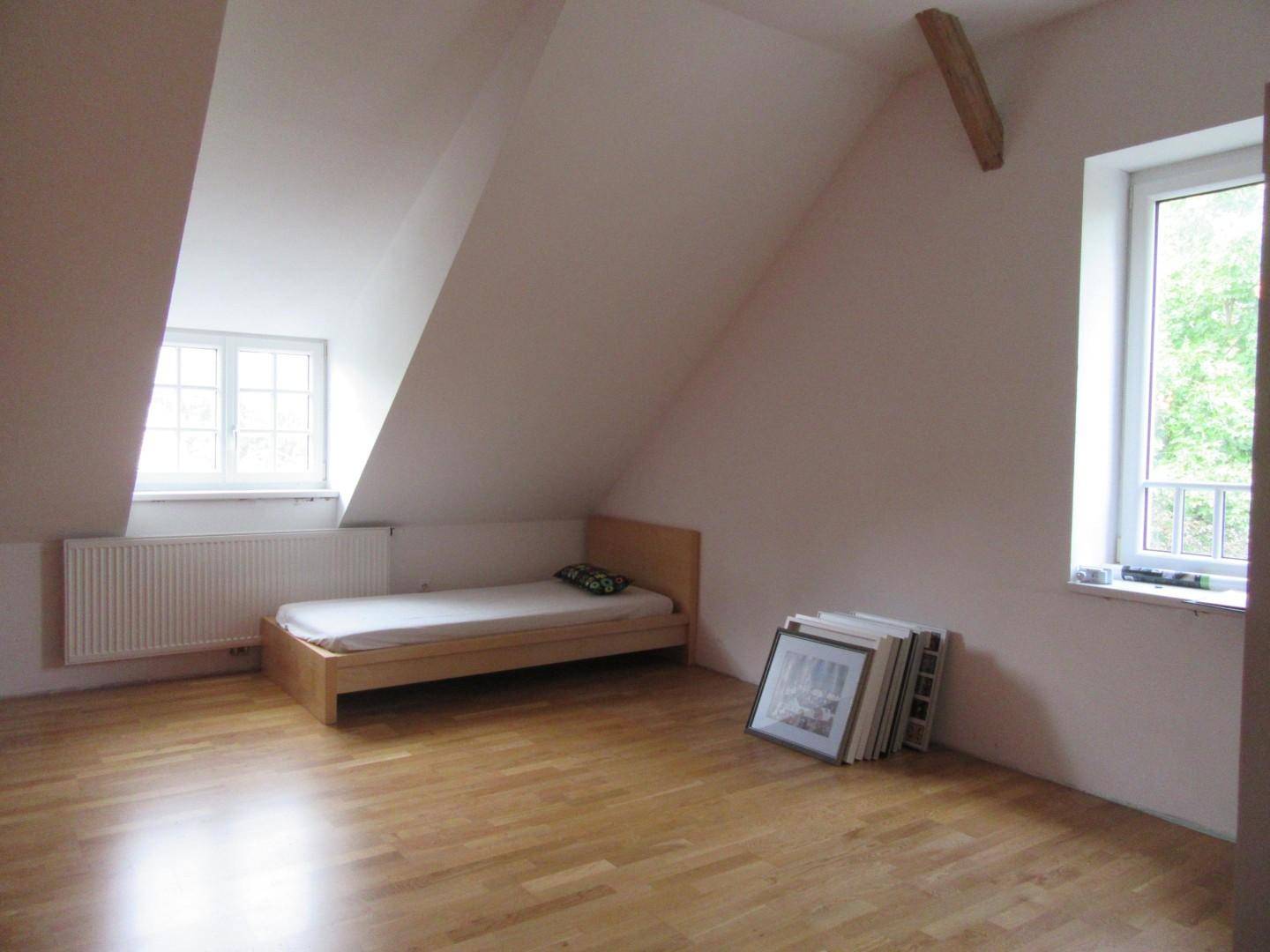 Helles Schlafzimmer im Dachgeschoss mit schrägen Wänden, Holzboden und einem Fenster.