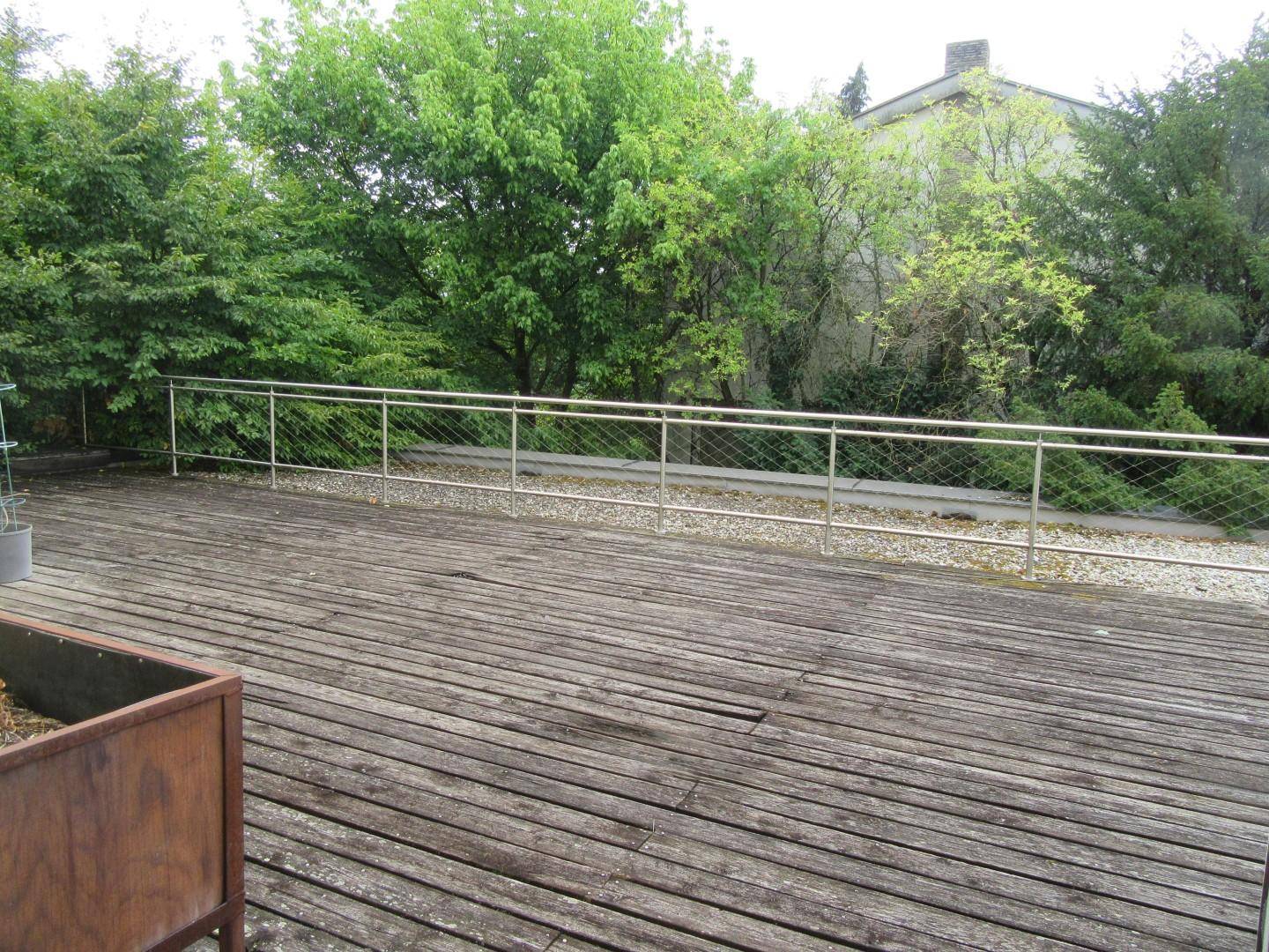 Große Holzterrasse mit Metallgeländer, umgeben von Bäumen und Sträuchern.