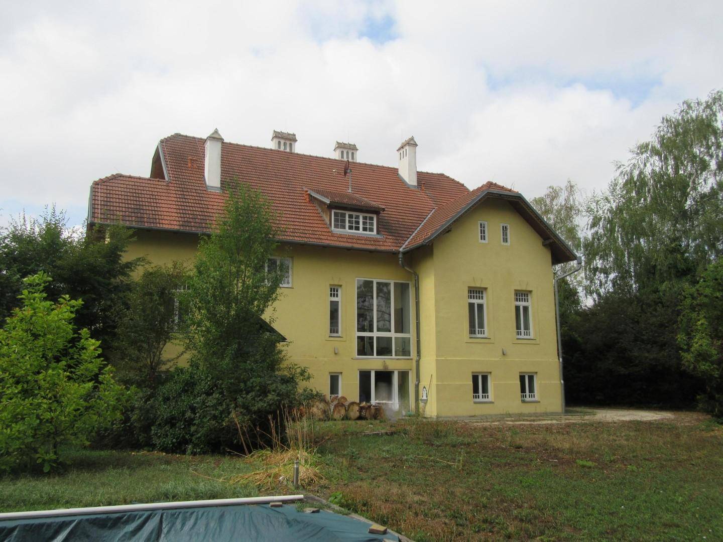 Rückansicht eines großen gelben Hauses mit rotem Dach und Garten, inklusive Poolbereich.