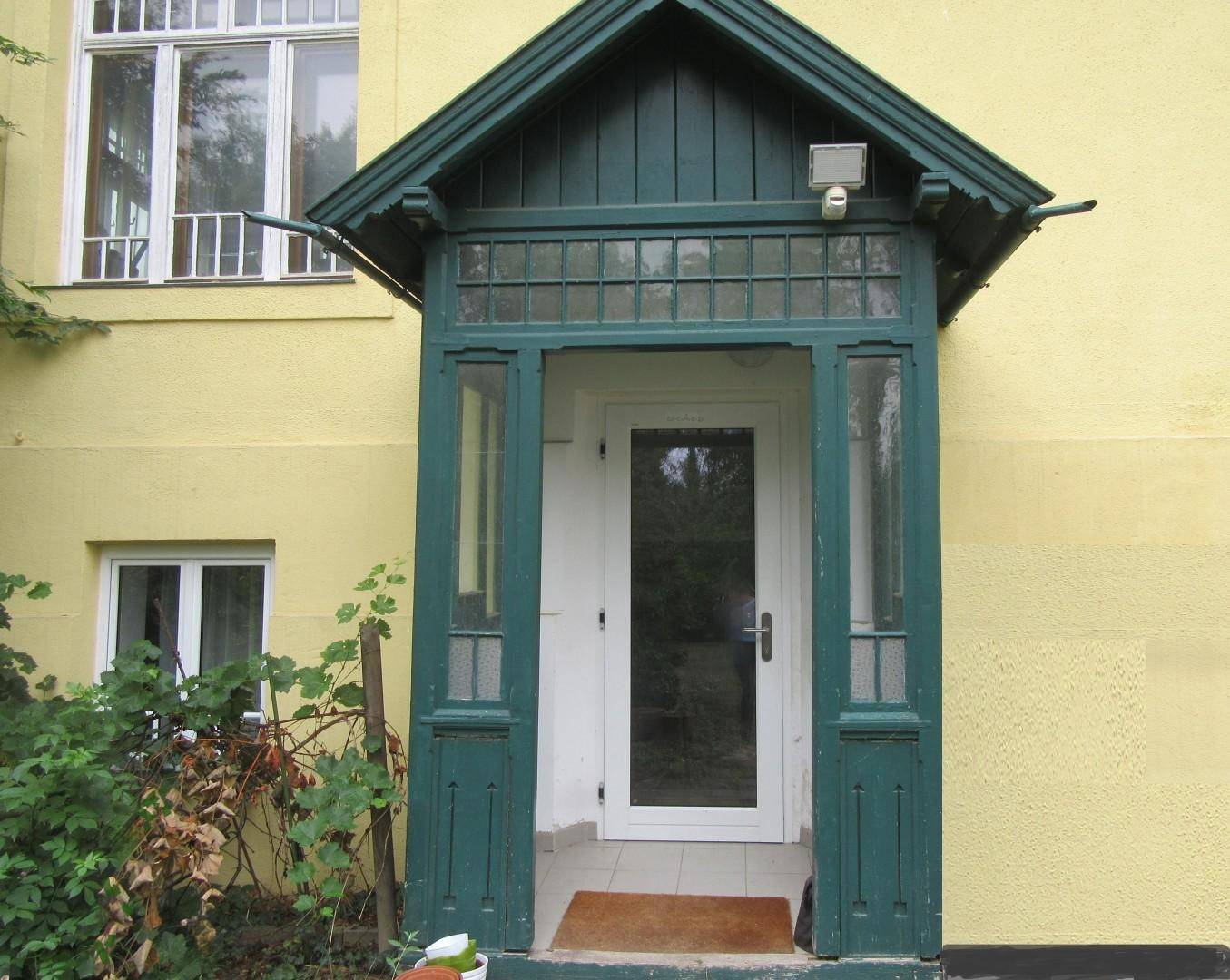 Grüner Eingangsbereich mit Vordach und Holzelementen, der zum Haus führt.