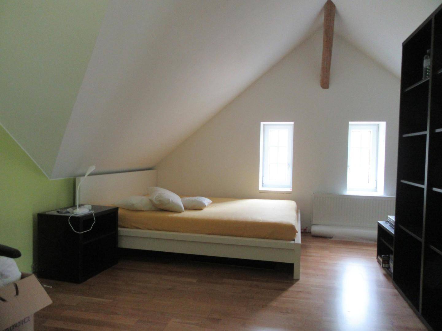 Gemütliches Schlafzimmer im Dachgeschoss mit schrägen Wänden, Holzboden und zwei Fenstern.