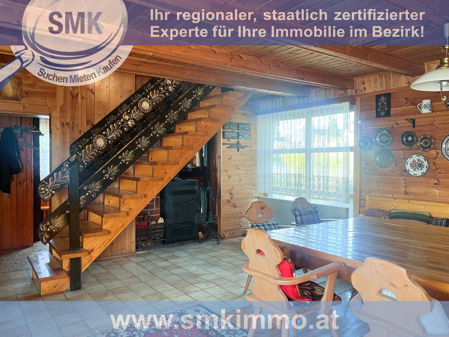 Rustikaler Wohn-Essbereich mit Holztisch, verzierter Treppe und Kachelofen.