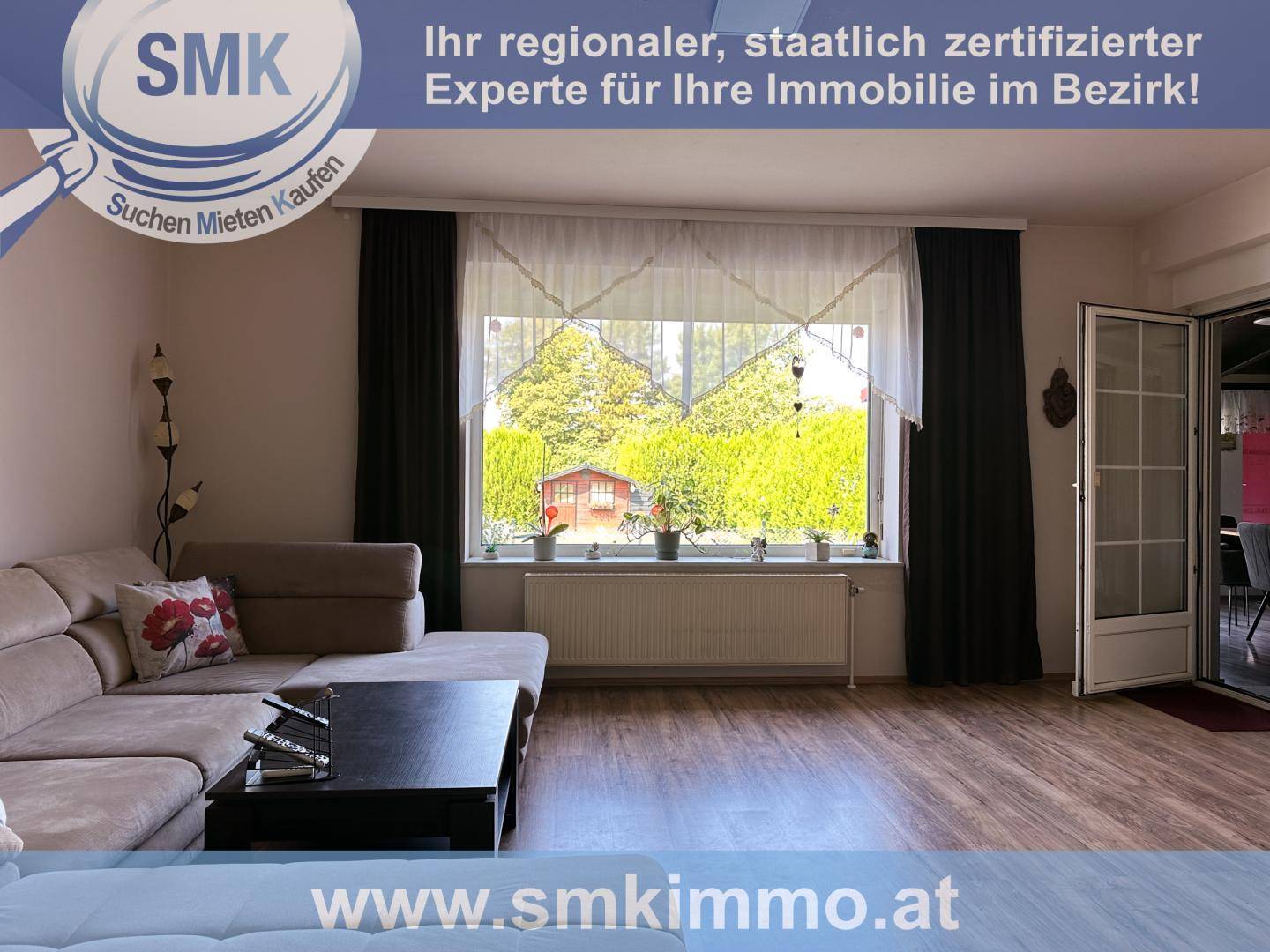 Gemütliches Wohnzimmer mit großem Fenster, Laminatboden und Zugang zum Außenbereich.