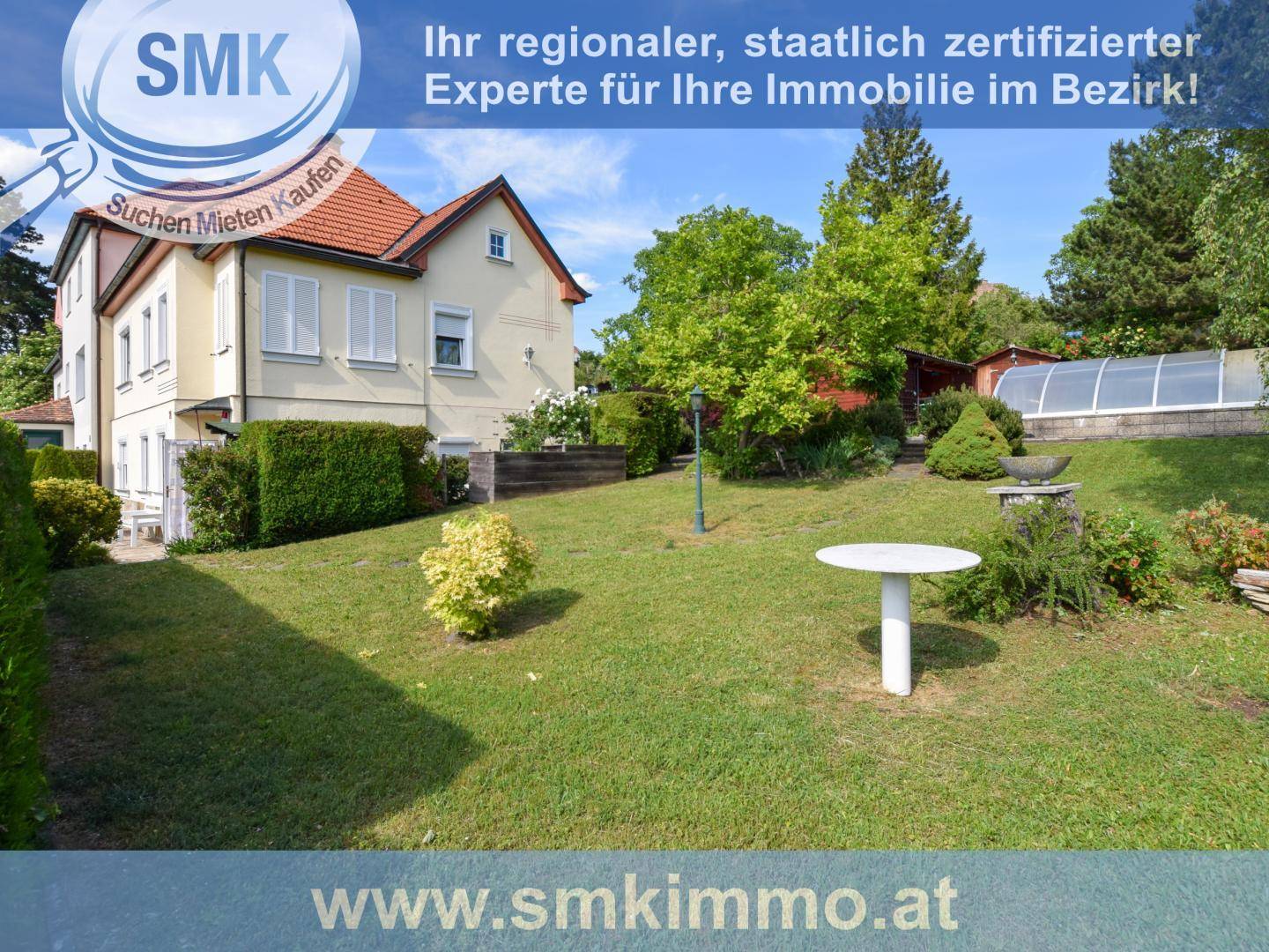 Gepflegter Rasenbereich vor einem Wohnhaus mit Hecken und einem kleinen Gartentisch.
