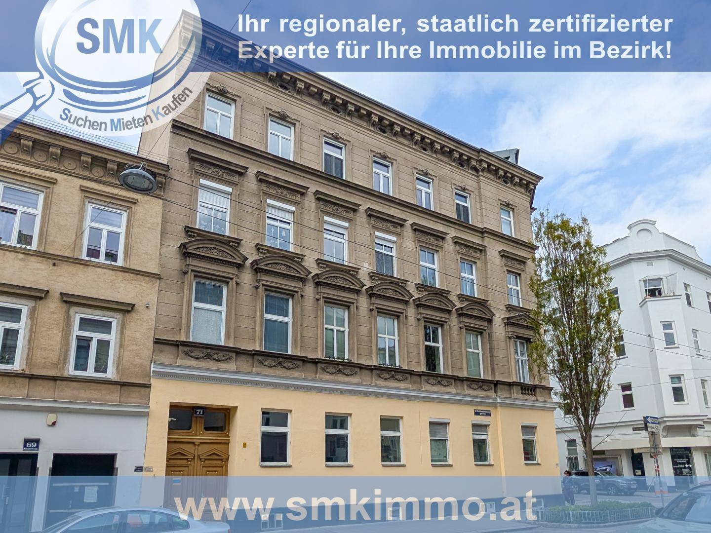 Historische Fassade eines Mehrfamilienhauses in städtischer Umgebung mit vielen Fenstern.