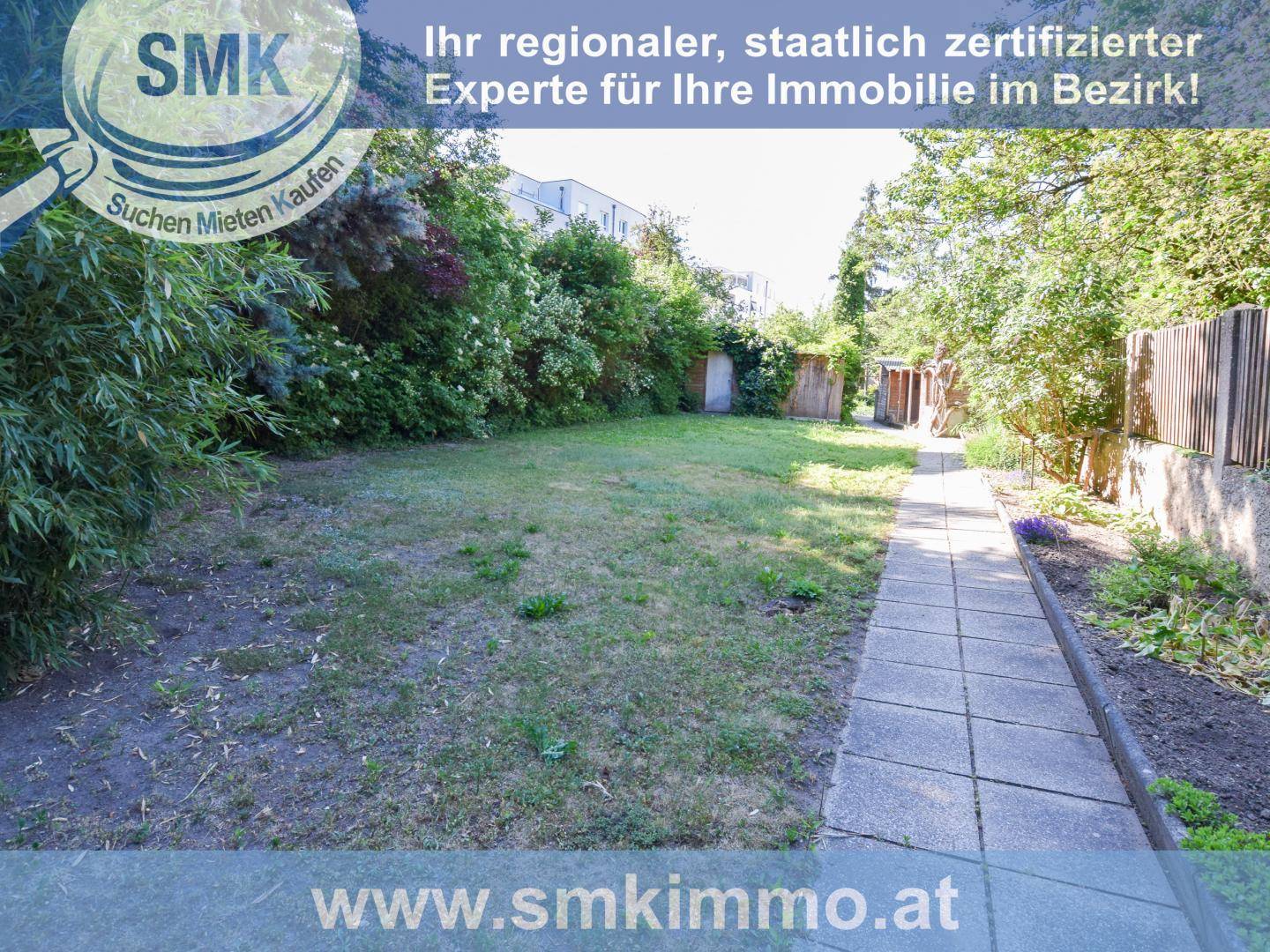 Gepflegter Gartenbereich mit Rasenfläche und einem gepflasterten Weg, umgeben von Bäumen und Sträuchern.