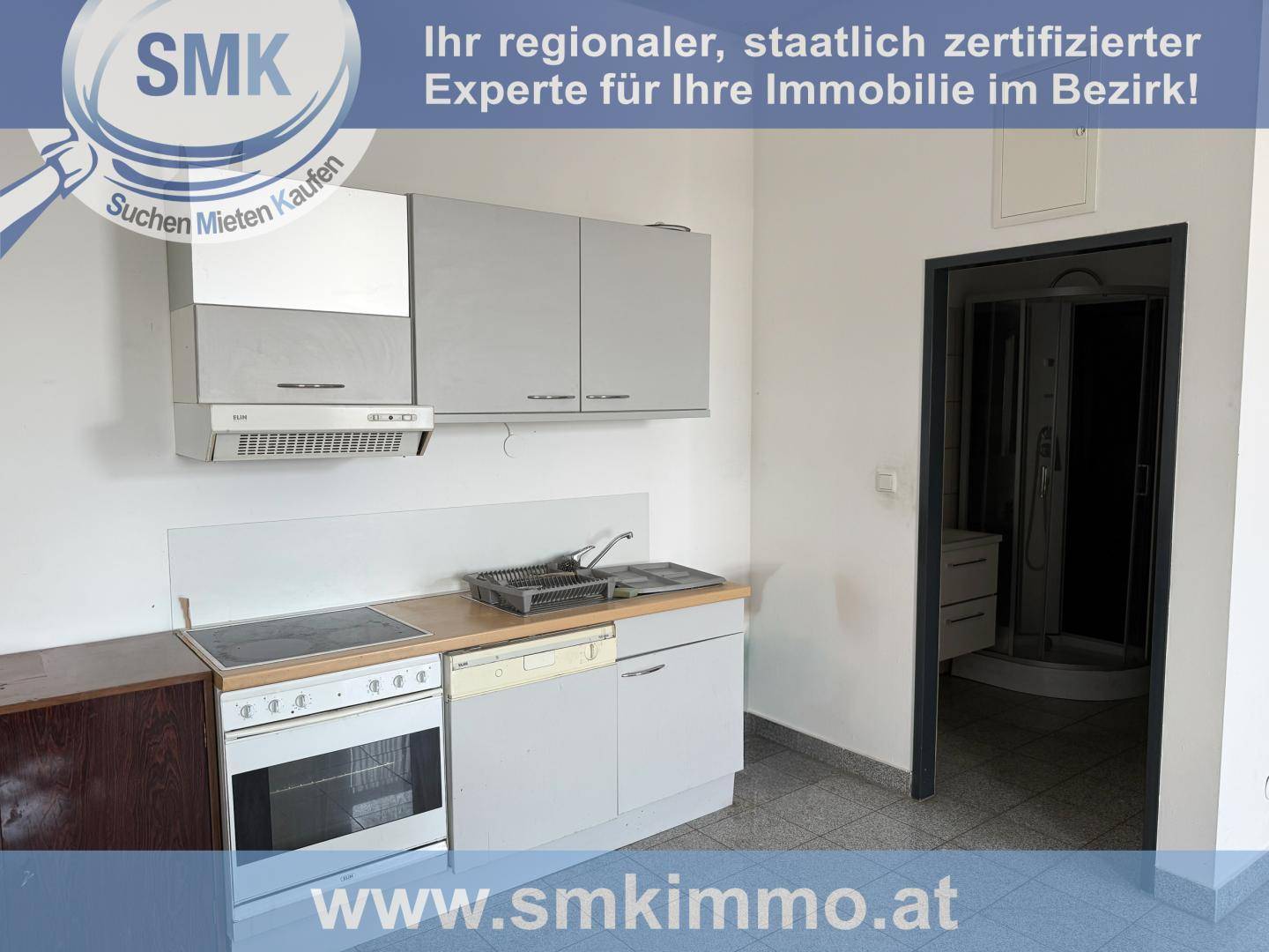 Kleine Küche mit grauen Schränken, Herd, Spüle und einem Durchgang zu einem angrenzenden Badezimmer.