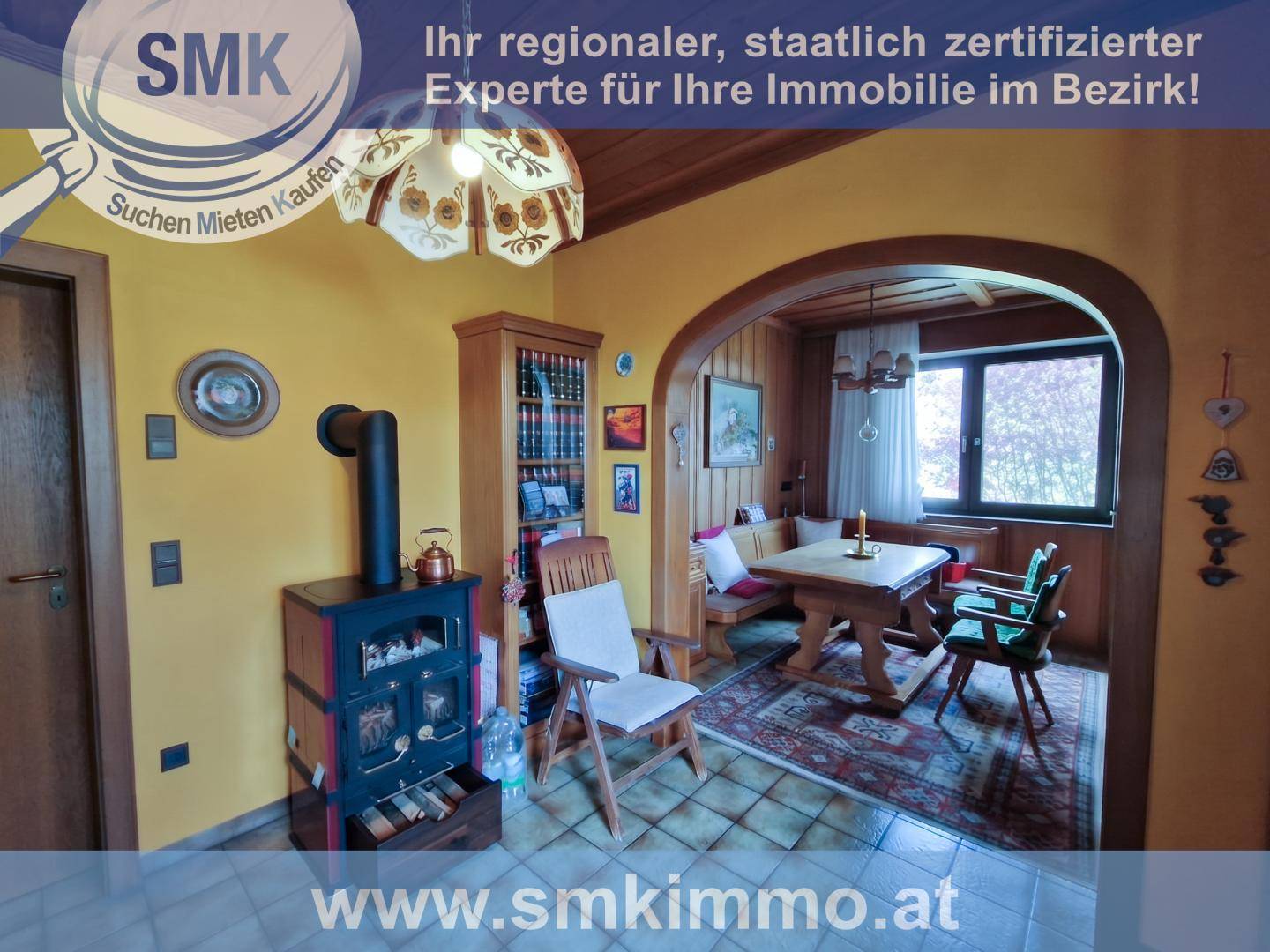 Gemütlicher Essbereich mit Kachelofen, Holztisch und Sitzbank, verbunden durch einen Bogen.