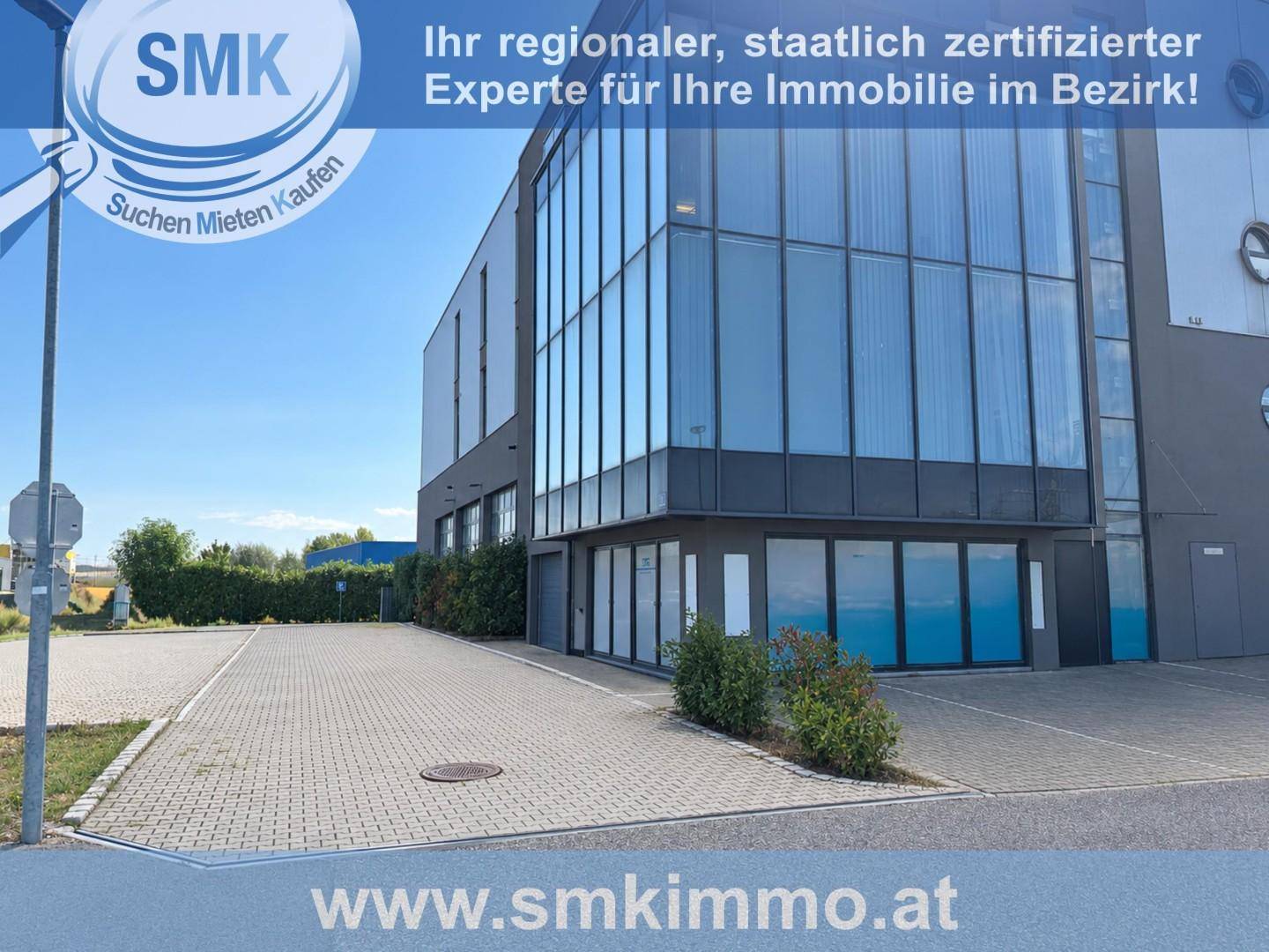 Moderne Geschäftsfassade mit großen Glasflächen und einem gepflasterten Parkplatz davor unter blauem Himmel.
