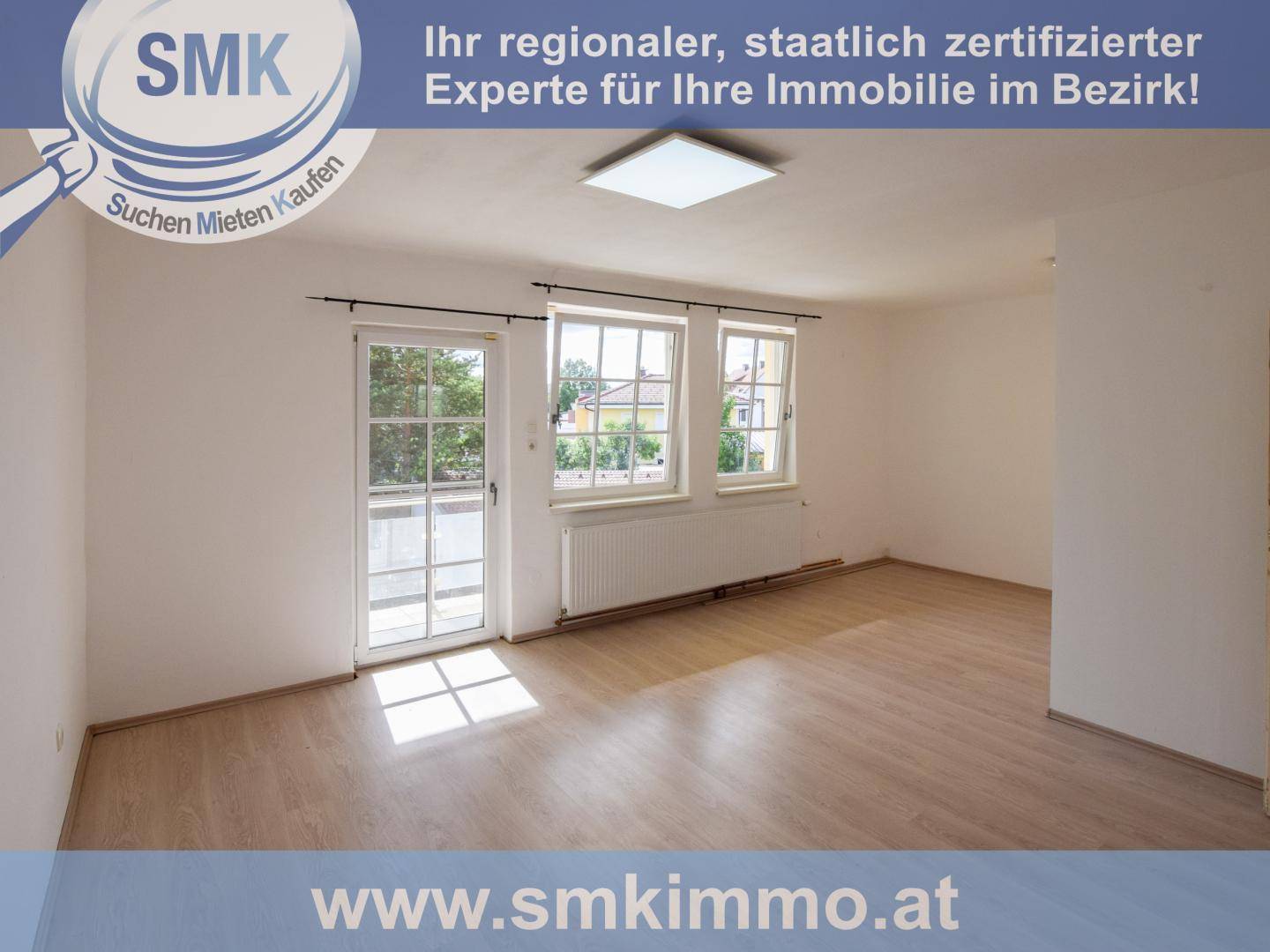 Heller, leerer Raum mit Laminatboden, großen Fenstern und Zugang zu einem Außenbereich.