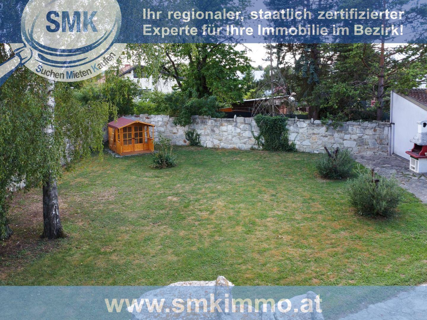 Großer, gepflegter Garten mit Rasenfläche, Steinmauer und kleinem Gartenhaus.