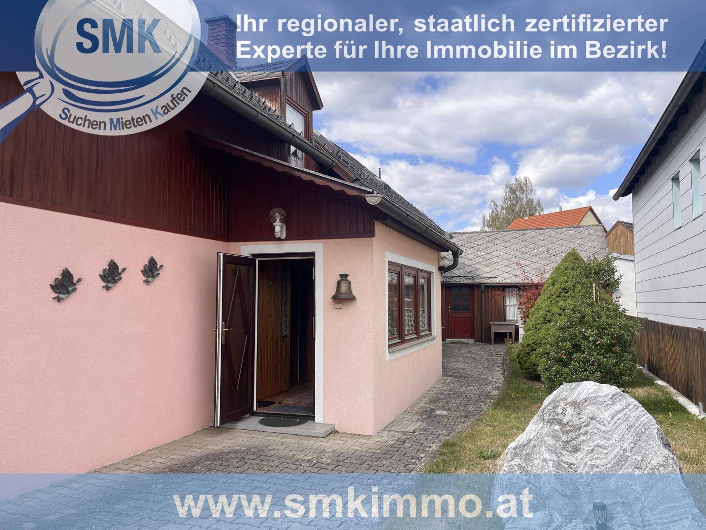 Eingangsbereich des Hauses mit rosa Fassade, Holzelementen und einem kleinen Vorgarten.