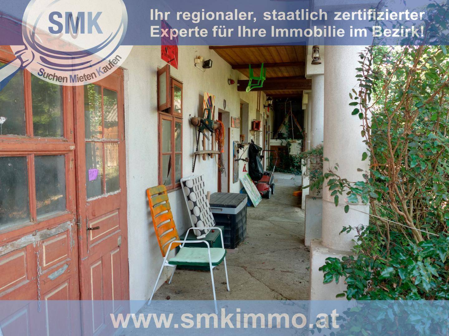 Überdachter Gang entlang der Hausrückseite mit rustikalen Säulen und Sitzgelegenheiten.