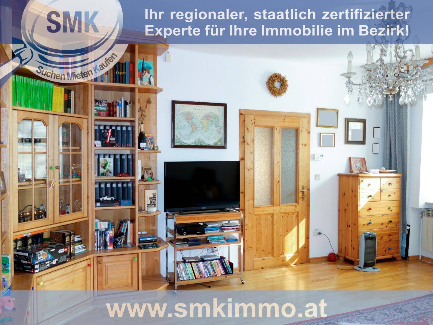 Wohnzimmer mit Holzbücherregal, Fernseher und klassischem Kronleuchter als Blickfang.