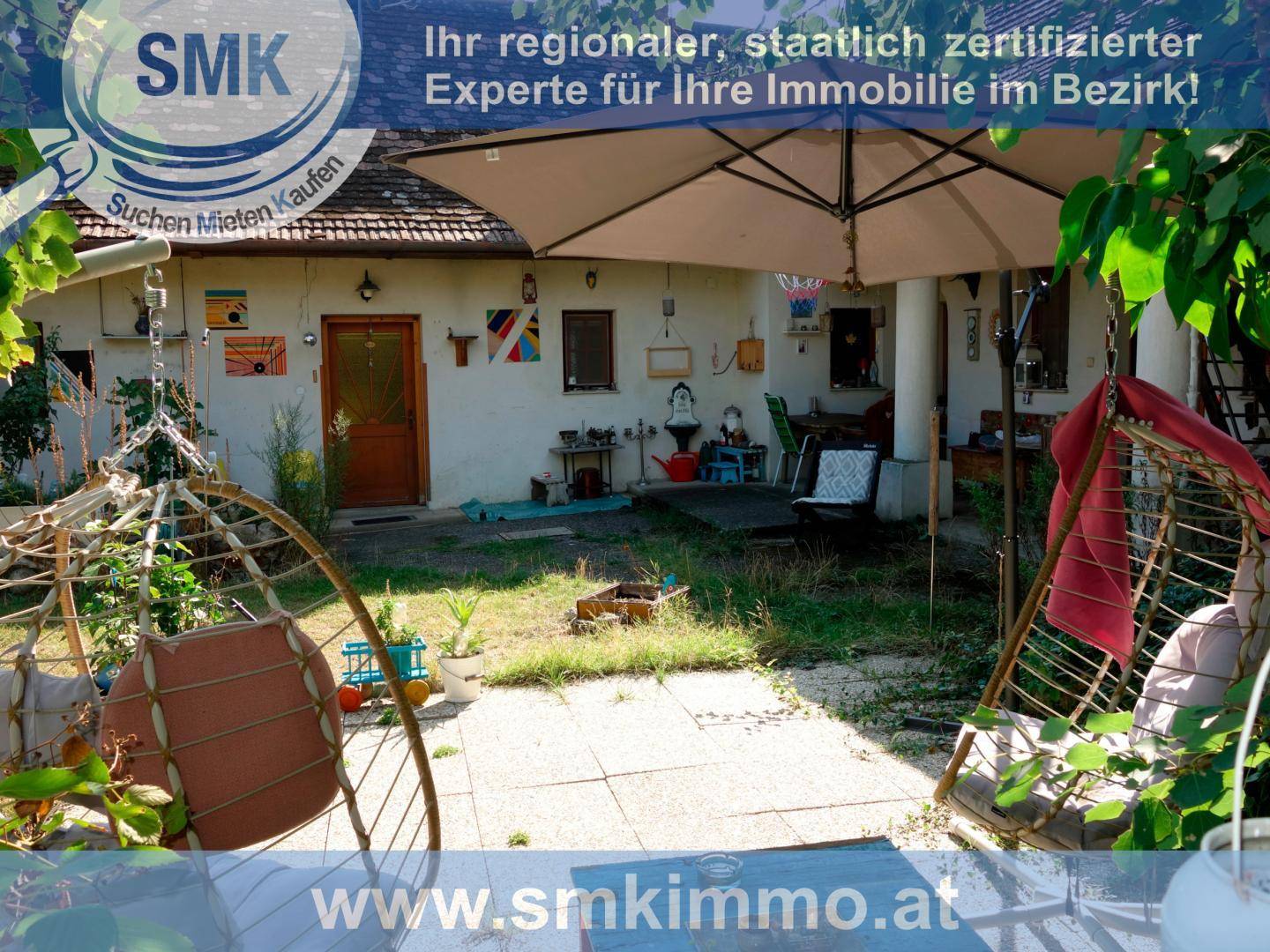 Gepflasterter Terrassenbereich mit zwei Hängesesseln und großem Sonnenschirm für entspannte Stunden.