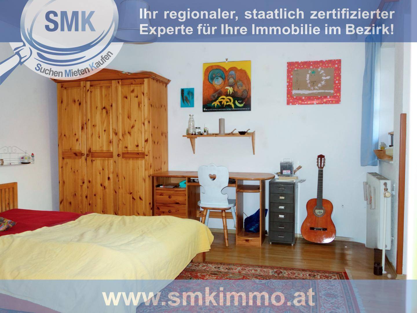 Schlafzimmer mit Holzkleiderschrank, Schreibtisch und einem Bett mit gelber Decke.