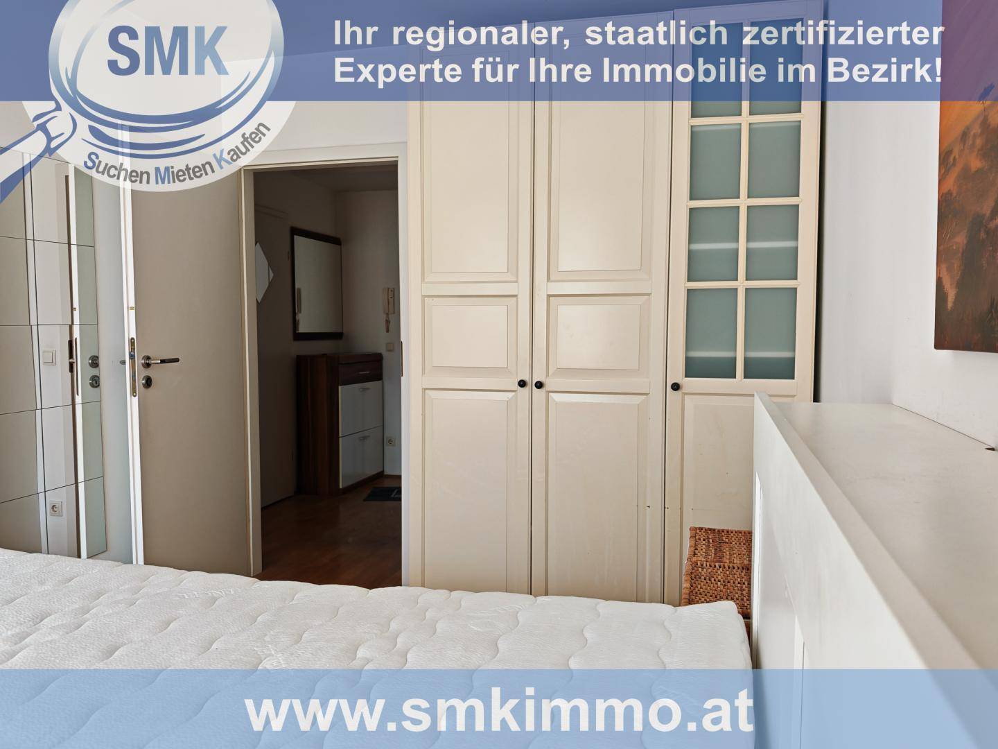 Schlafzimmer mit großem weißen Kleiderschrank und Blick in den angrenzenden Flurbereich.