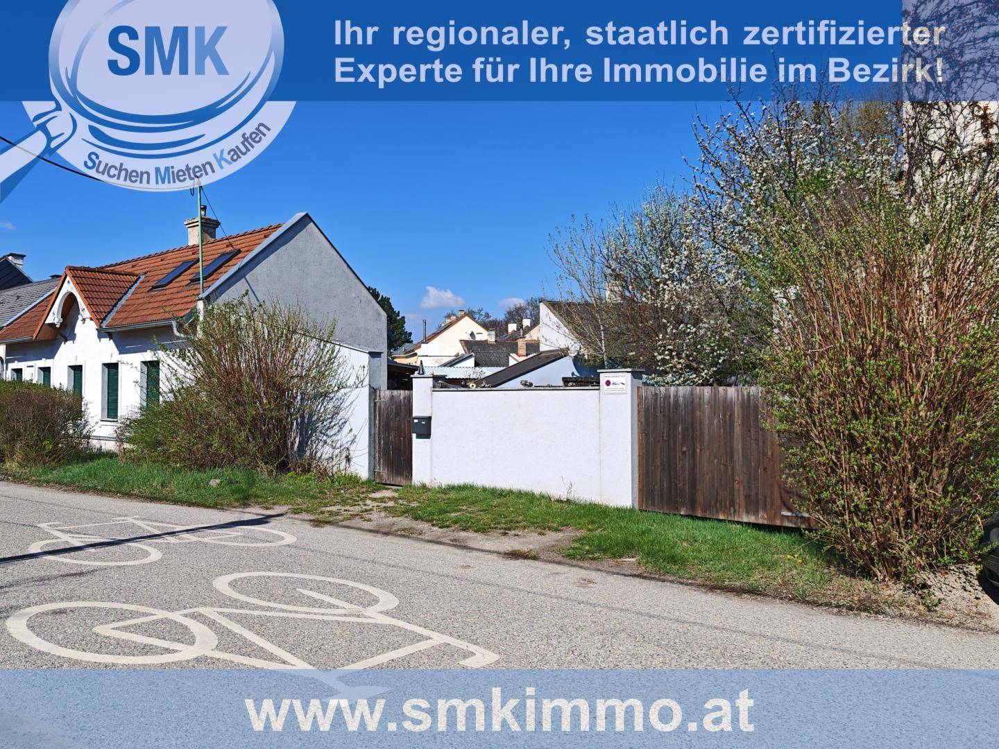 Außenansicht eines Hauses von der Straße aus, umgeben von einem Zaun und Büschen.