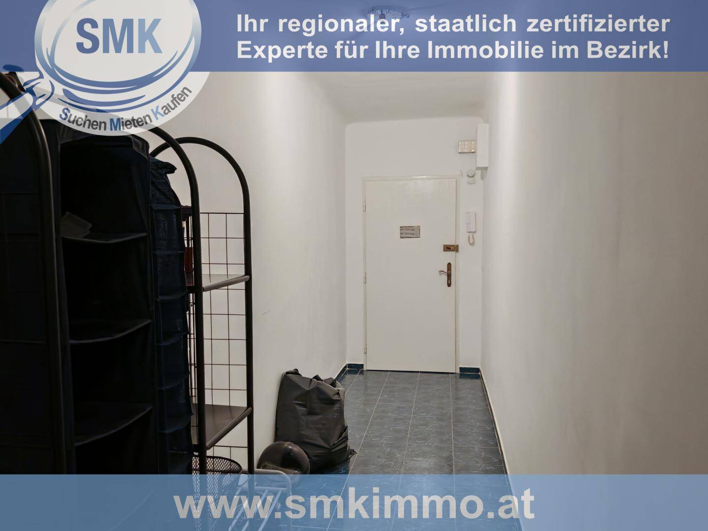 Schmaler Flur mit dunklen Fliesen, Schuhregal und der Eingangstür der Wohnung.