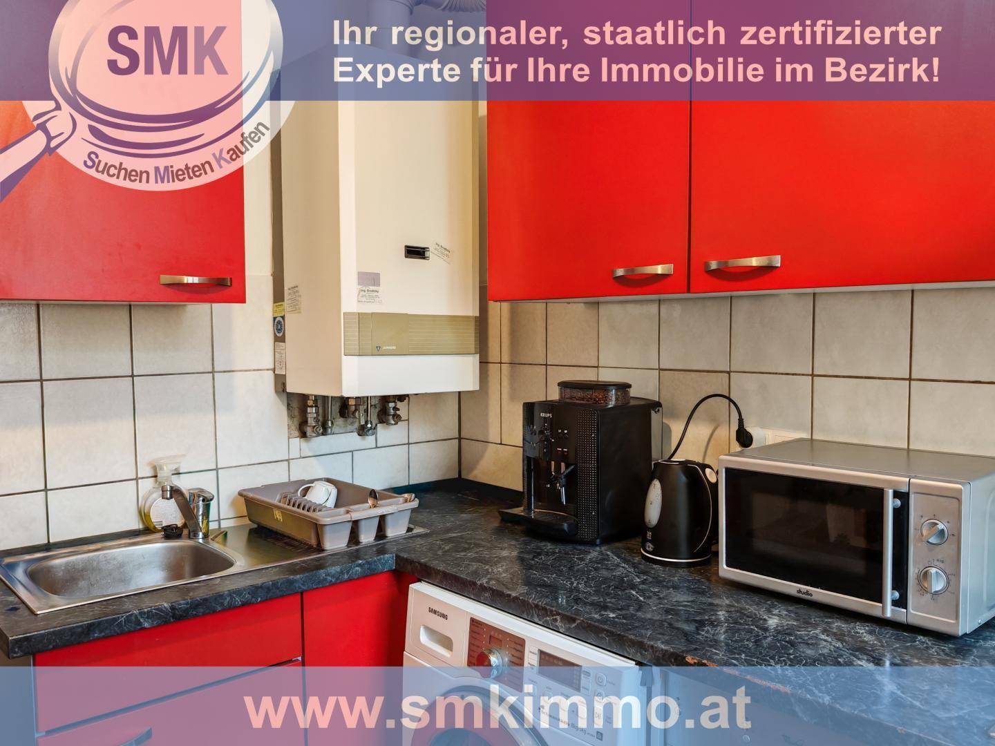 Küche mit roten Schränken, Spüle, Mikrowelle und Warmwasserbereiter an der Wand.