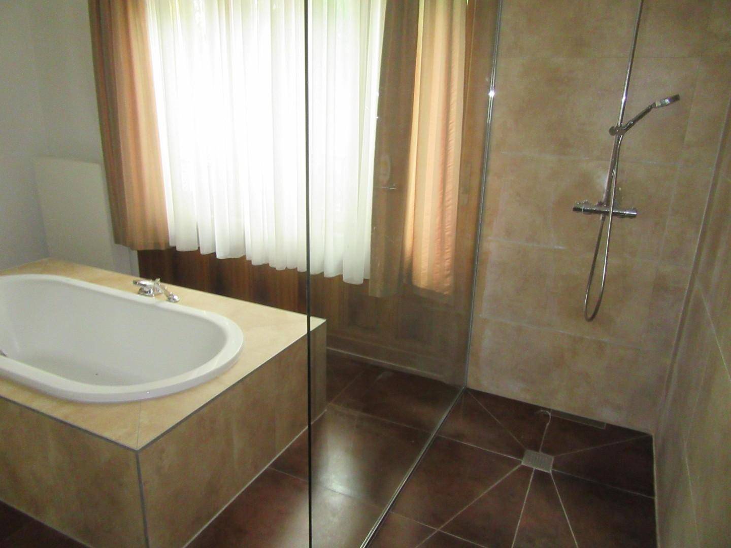 Helles Badezimmer mit Badewanne, Duschbereich und Fenster, ausgestattet mit beigen Fliesen.
