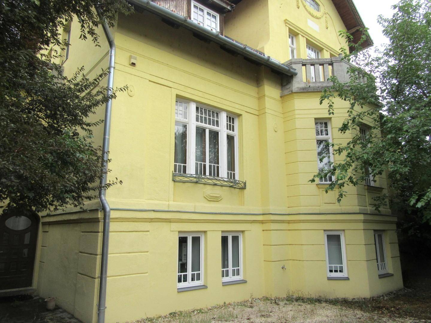 Gelbe Fassade eines historischen Gebäudes mit vielen Fenstern und einem kleinen Balkon.