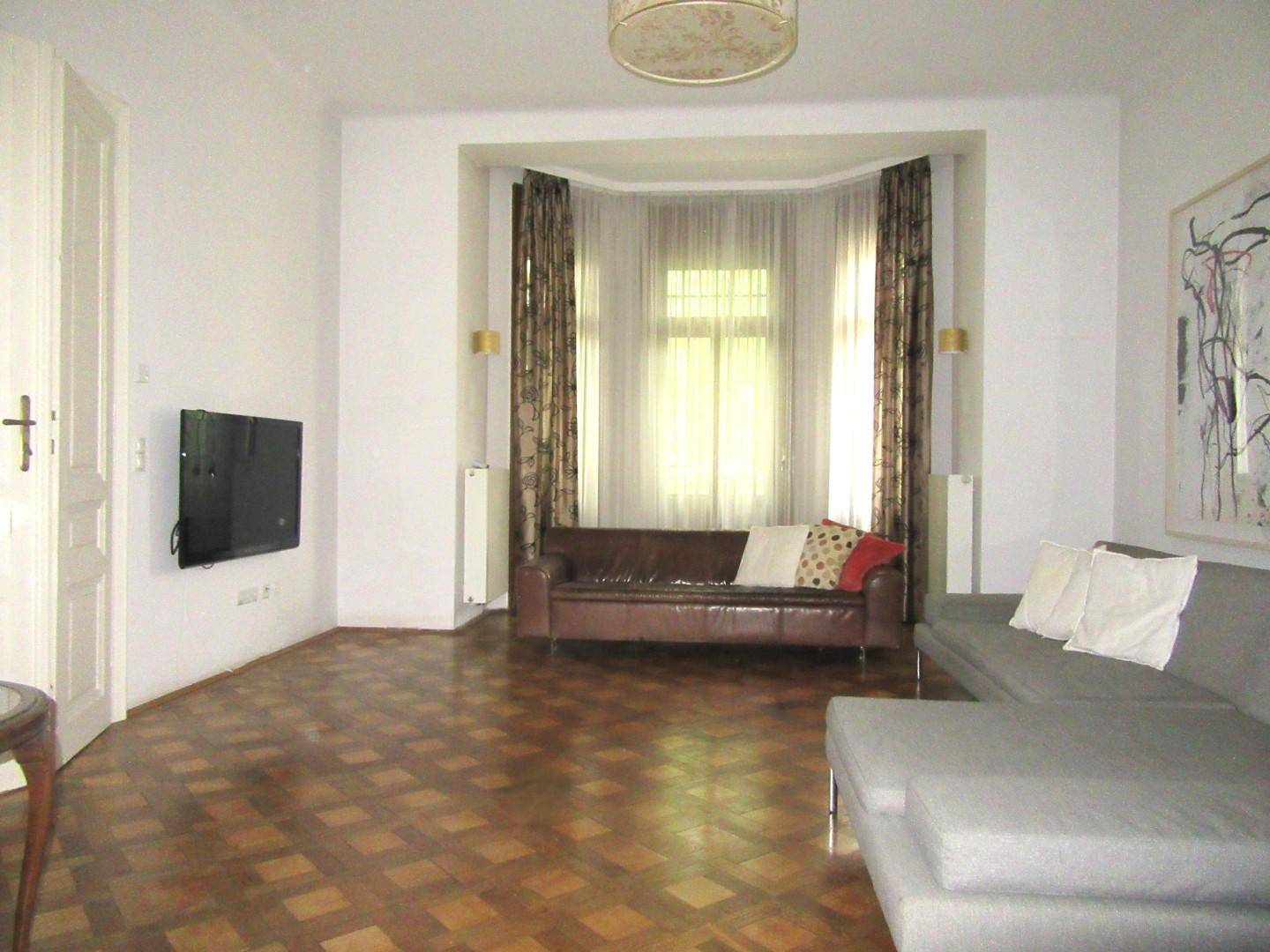 Gemütliches Wohnzimmer mit Parkettboden, bequemen Sofas und einem Erkerfenster mit Vorhängen.