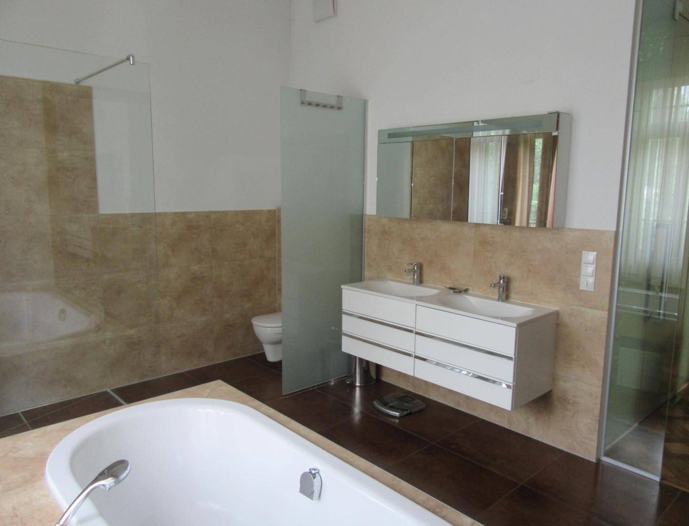 Modernes Badezimmer mit Doppelwaschbecken, Badewanne und begehbarer Dusche, teilweise gefliest.