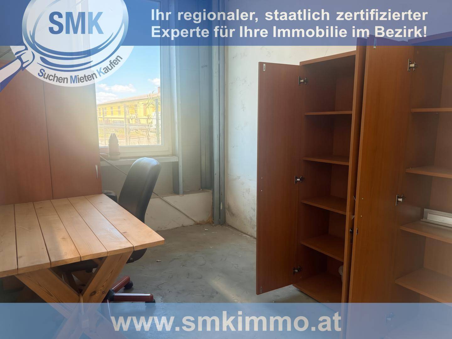 Einfacher Büroraum mit Holztisch, Bürostuhl und offenem Schrank, mit Blick nach draußen.