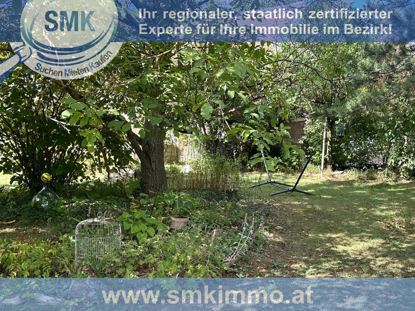 Großer Garten mit altem Baum, Rasenfläche und dekorativem Vogelkäfig.