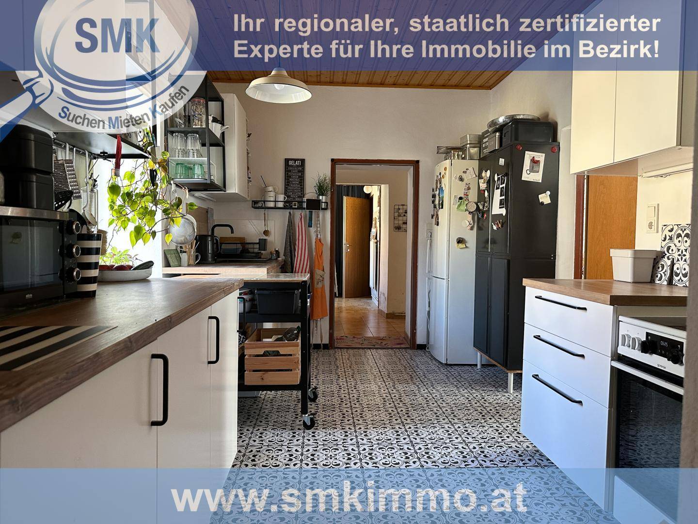Praktische Küche mit Kühlschrank, weißen Schränken und gemusterten Bodenfliesen.