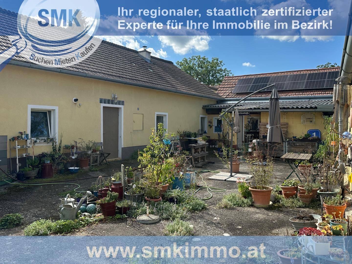 Geräumiger Innenhof mit vielfältiger Bepflanzung, Sonnenschirm und Solaranlage auf dem Dach.