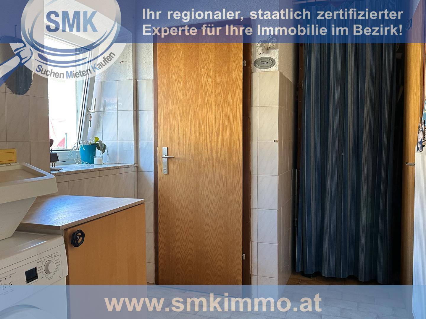 Badezimmer mit Waschmaschine, Holztür und Duschbereich hinter einem Vorhang.