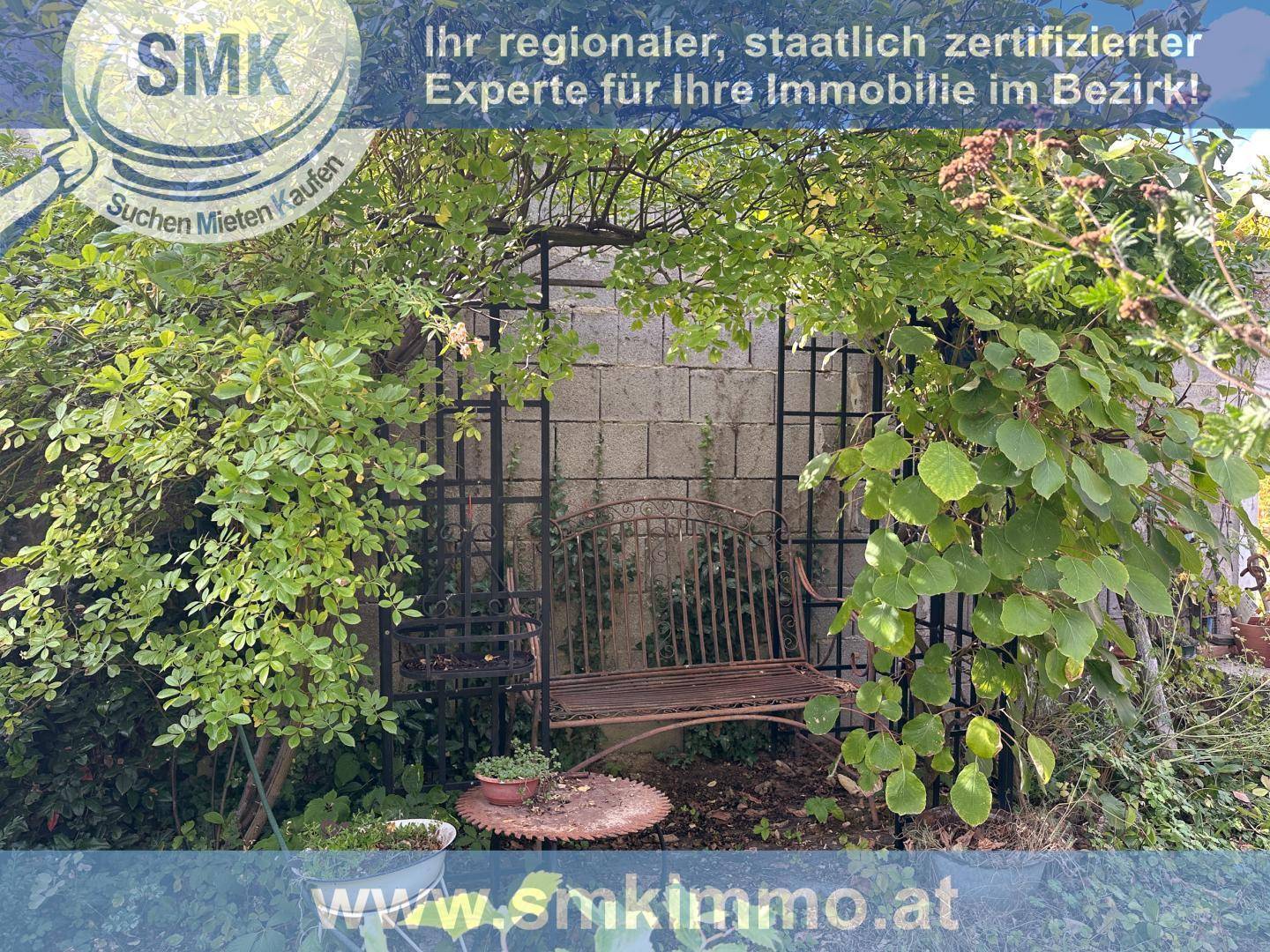 Romantischer Gartenbereich mit einer Metallbank unter einem bewachsenen Rankbogen.