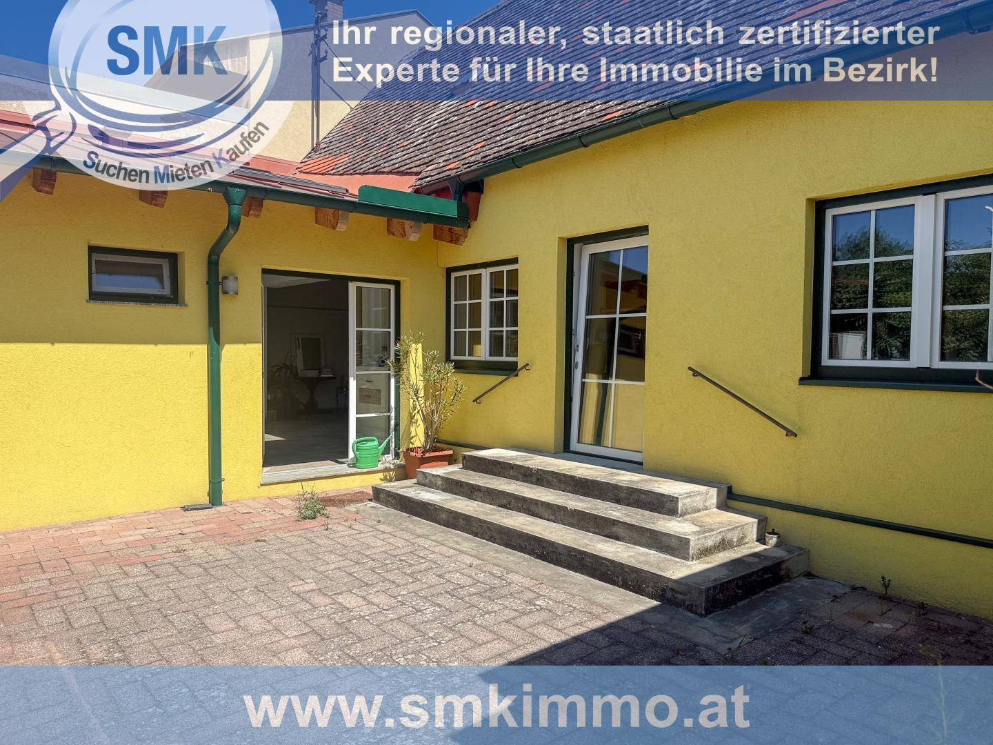 Gelbes Haus mit gepflasterter Terrasse und Stufen, die zum Eingangsbereich führen.